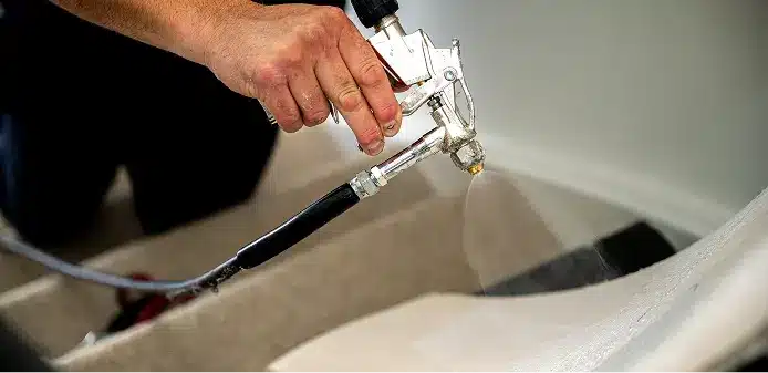 Lijm aanbrengen op de traptrede Hand met een chromen spuitpistool brengt lijm aan op een beklede traptrede