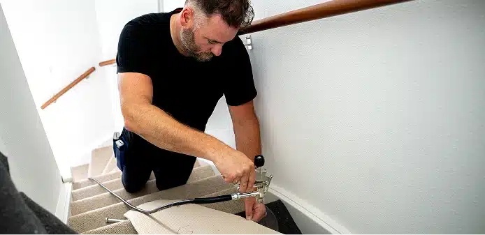 Stoffeerder knielt op een beklede trap en brengt met een spuitpistool lijm aan langs de wand