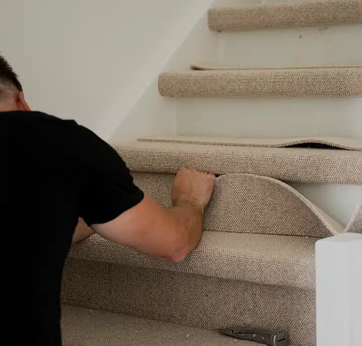 Stoffeerder werkt aan de trapbekleding, met een opengeklapt stanleymes op de onderste trede